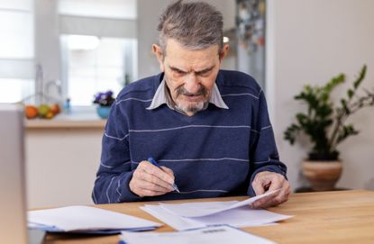 A senior adult man sitting at a table stacked with papers
