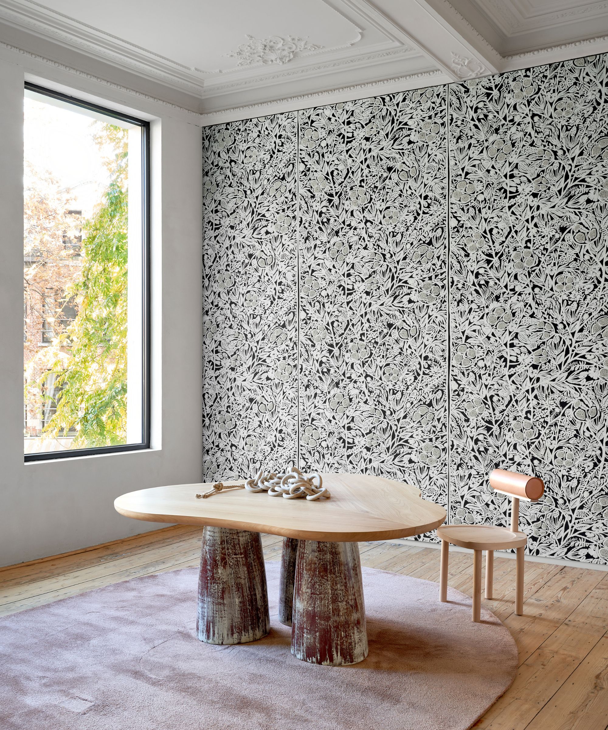 A room with a large window, a wall covering on one side and a modern curved oak table and chair in the centre