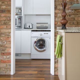 Door looking into a utility room with white washing machine, bread bin, toaster, and microwave