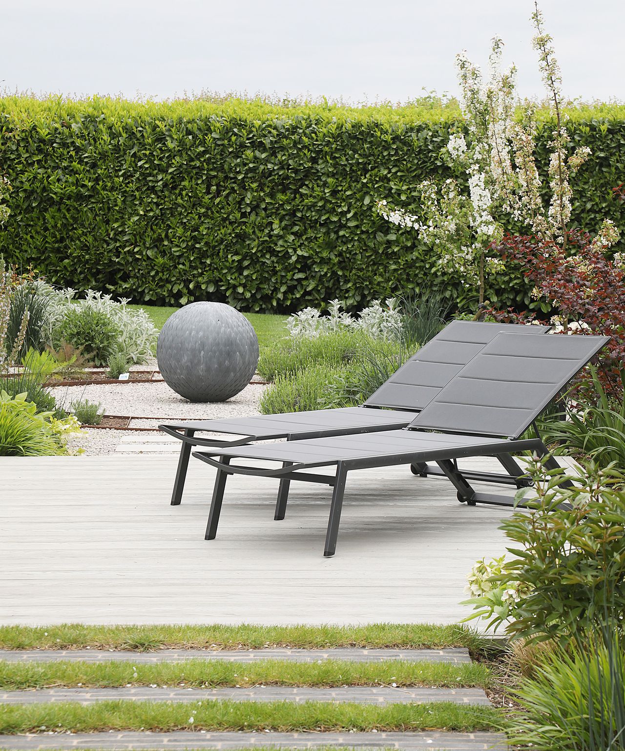 Two sun loungers on a newly landscaped decking area of a garden with a garden sculpture and clipped hedge