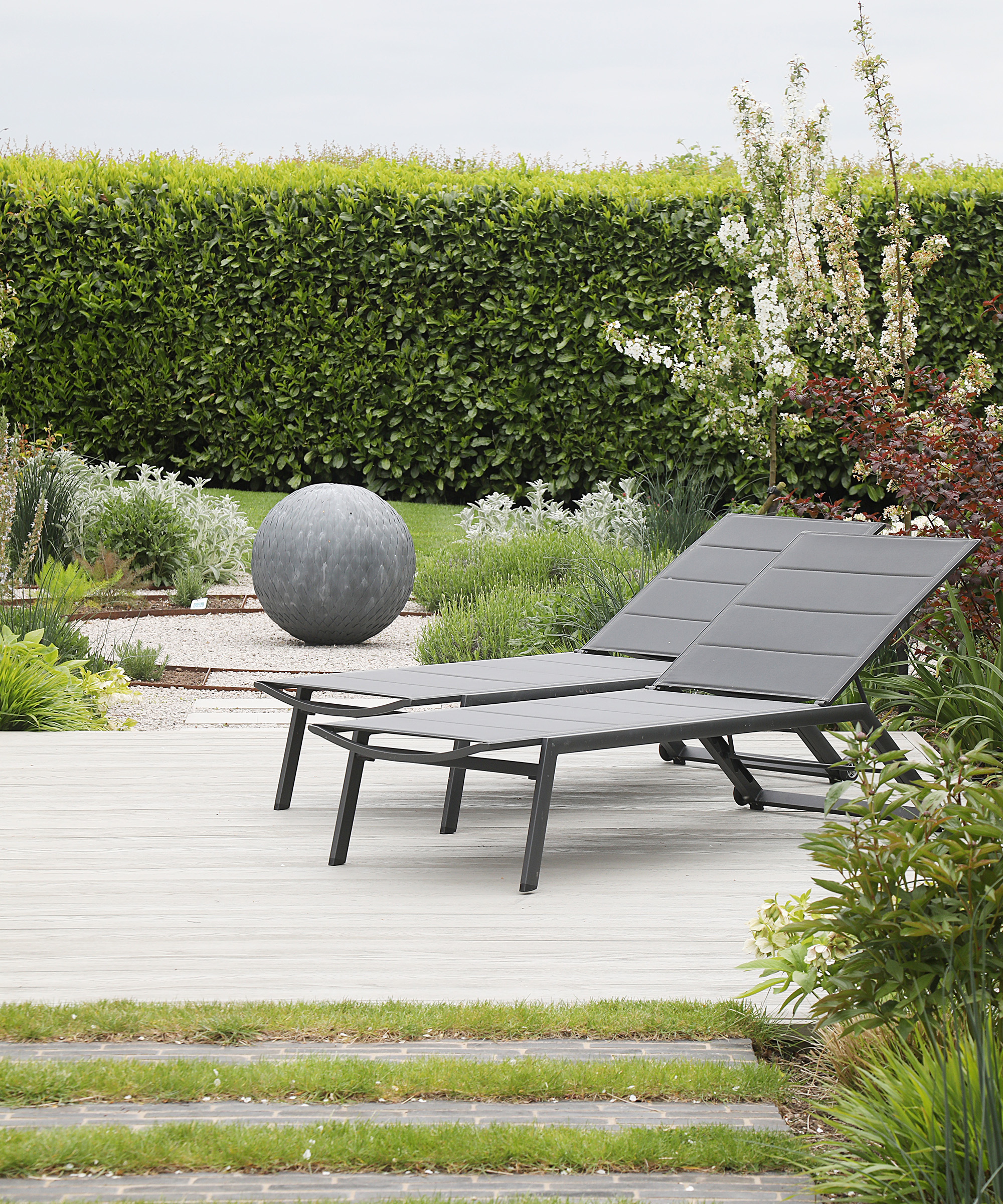Two sun loungers on a newly landscaped decking area of a garden with a garden sculpture and clipped hedge