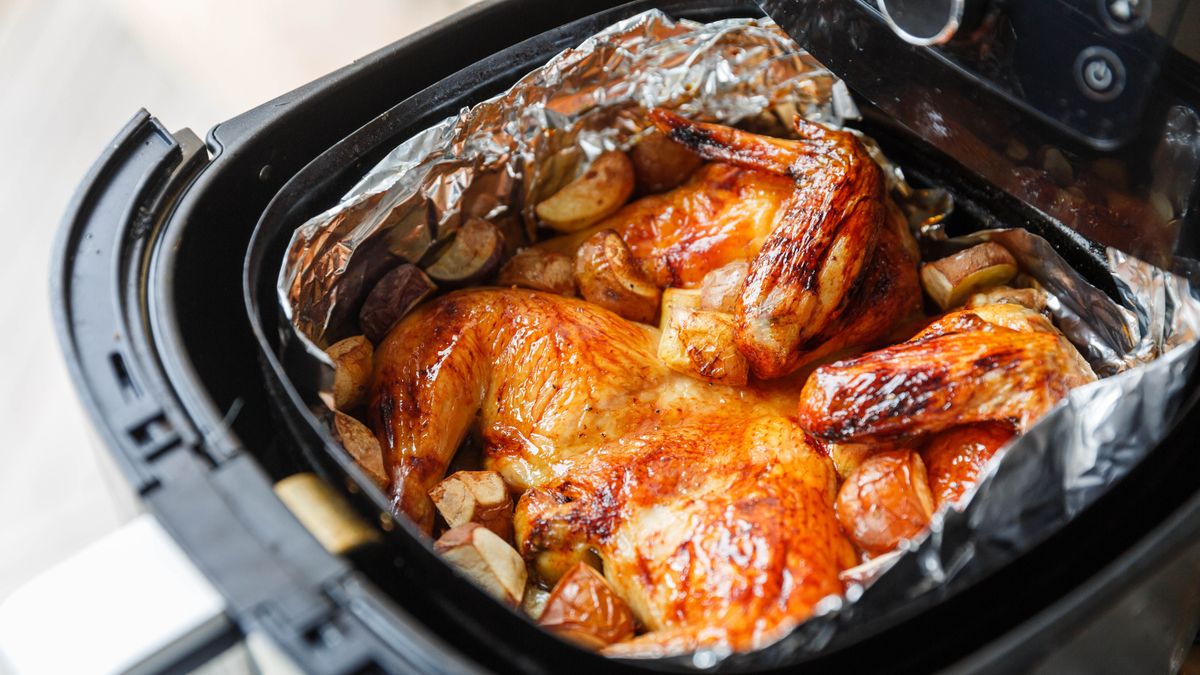 A chicken with potatoes in an air fryer basket