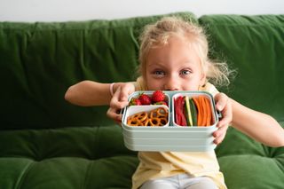 Girl with lunch box filled with vegetables and berries