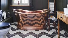 small bathroom with black and white zigzag floor tiles and brass freestanding rolltop bath