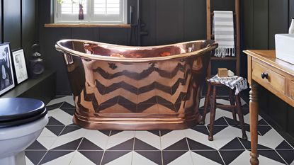 small bathroom with black and white zigzag floor tiles and brass freestanding rolltop bath