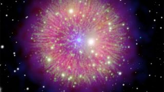 a small, bright blue central dot erupts with rays of brilliant pink and yellow-green, with shining stars dispersed within as well as around in the black of space.
