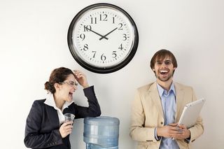 Two office workers laugh around the water cooler. 
