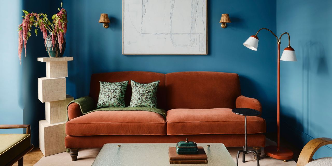 living room with blue walls, orange sofa, plinth with flowers, floor lamp, and glass coffee table