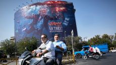 Motorcyclists in Tehran pass a billboard depicting U.S. President Donald Trump underwater amid explosions.