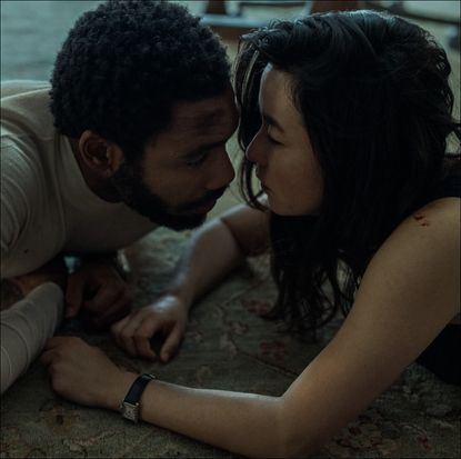 a man (donald glover as john smith) and a woman (maya erskine as jane smith) look at each other while lying on a floor