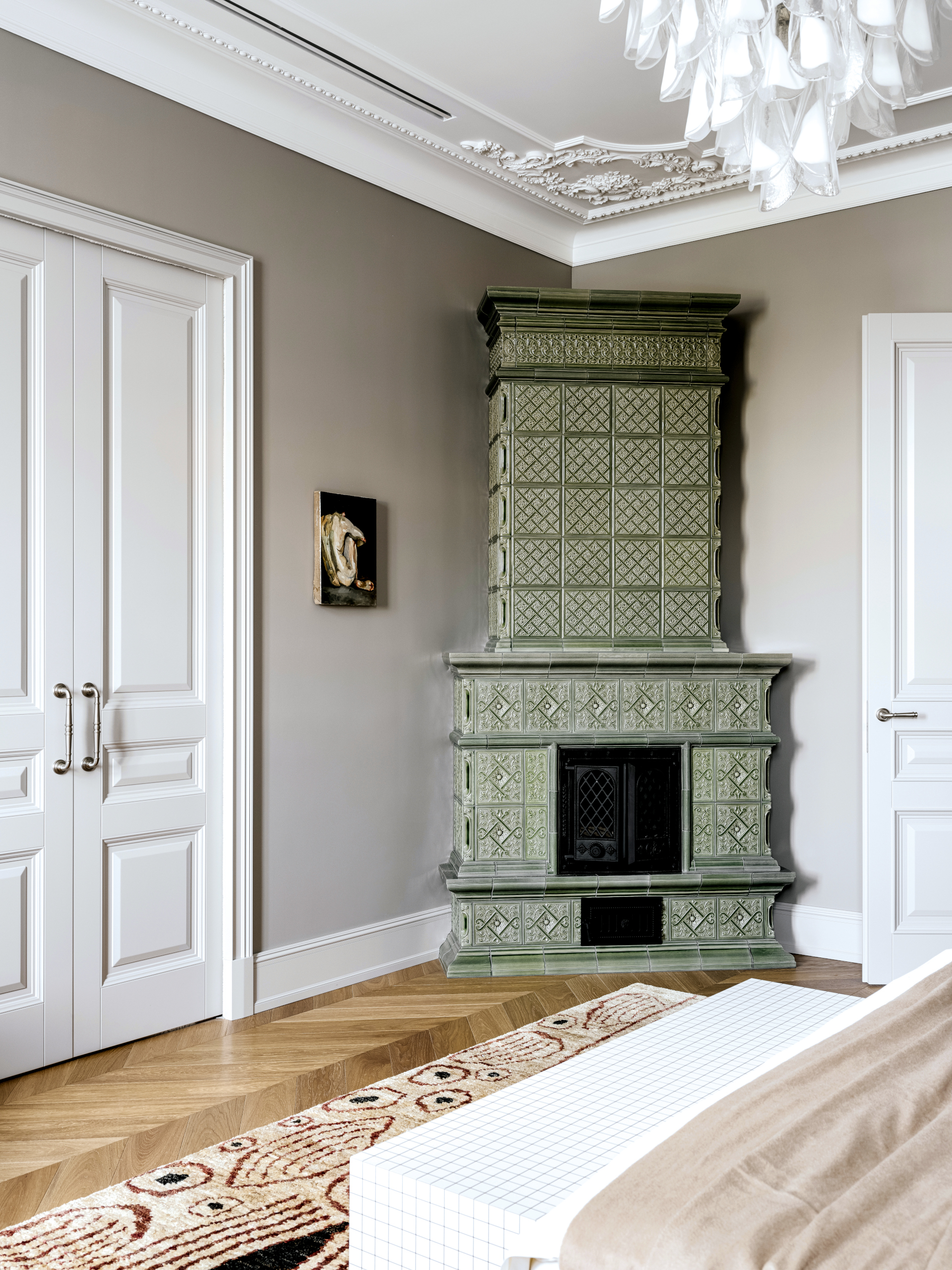Sage-green ceramic stove in the corner of a pale gray bedroom