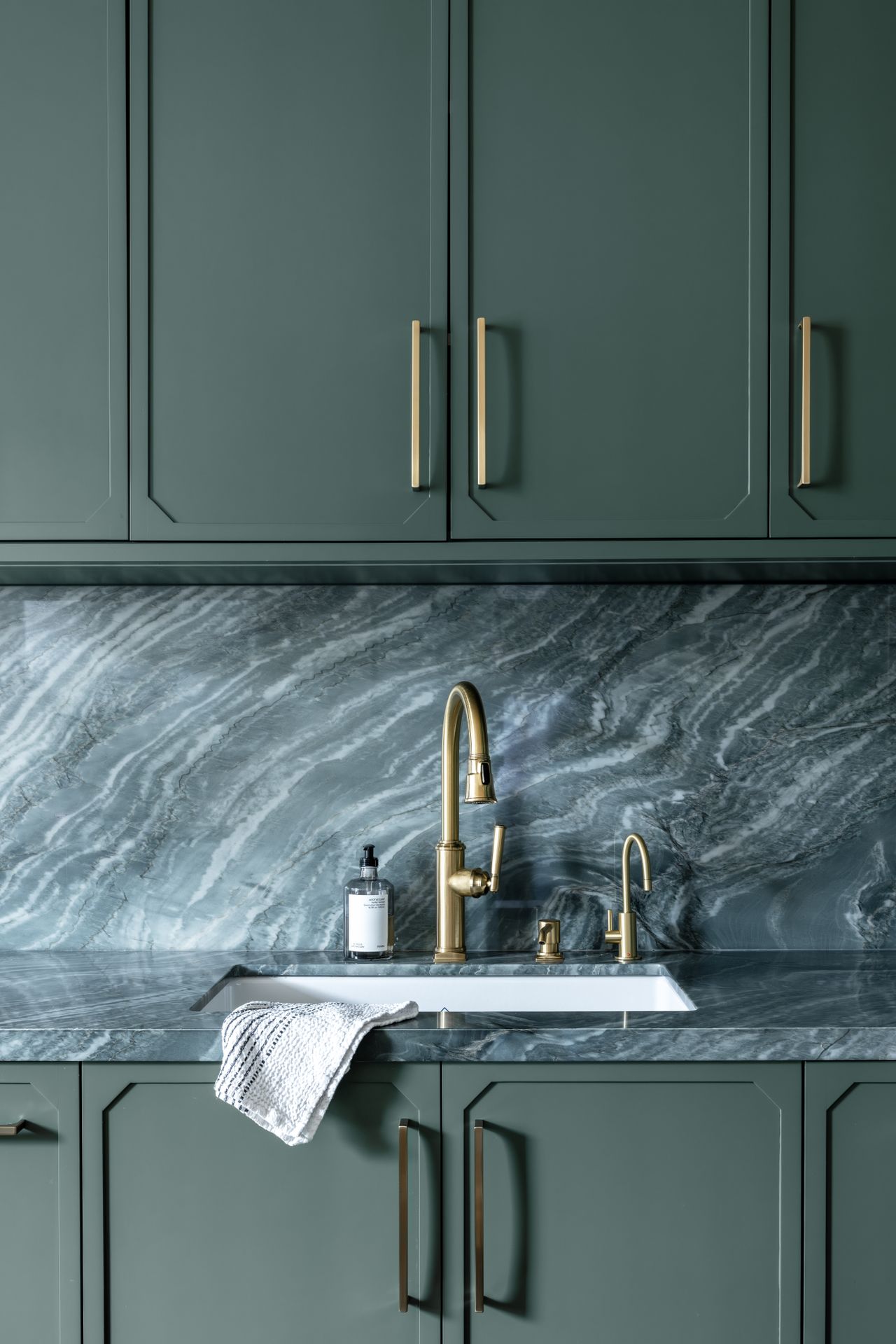 A kitchen with deep green cabinets and brass hadware