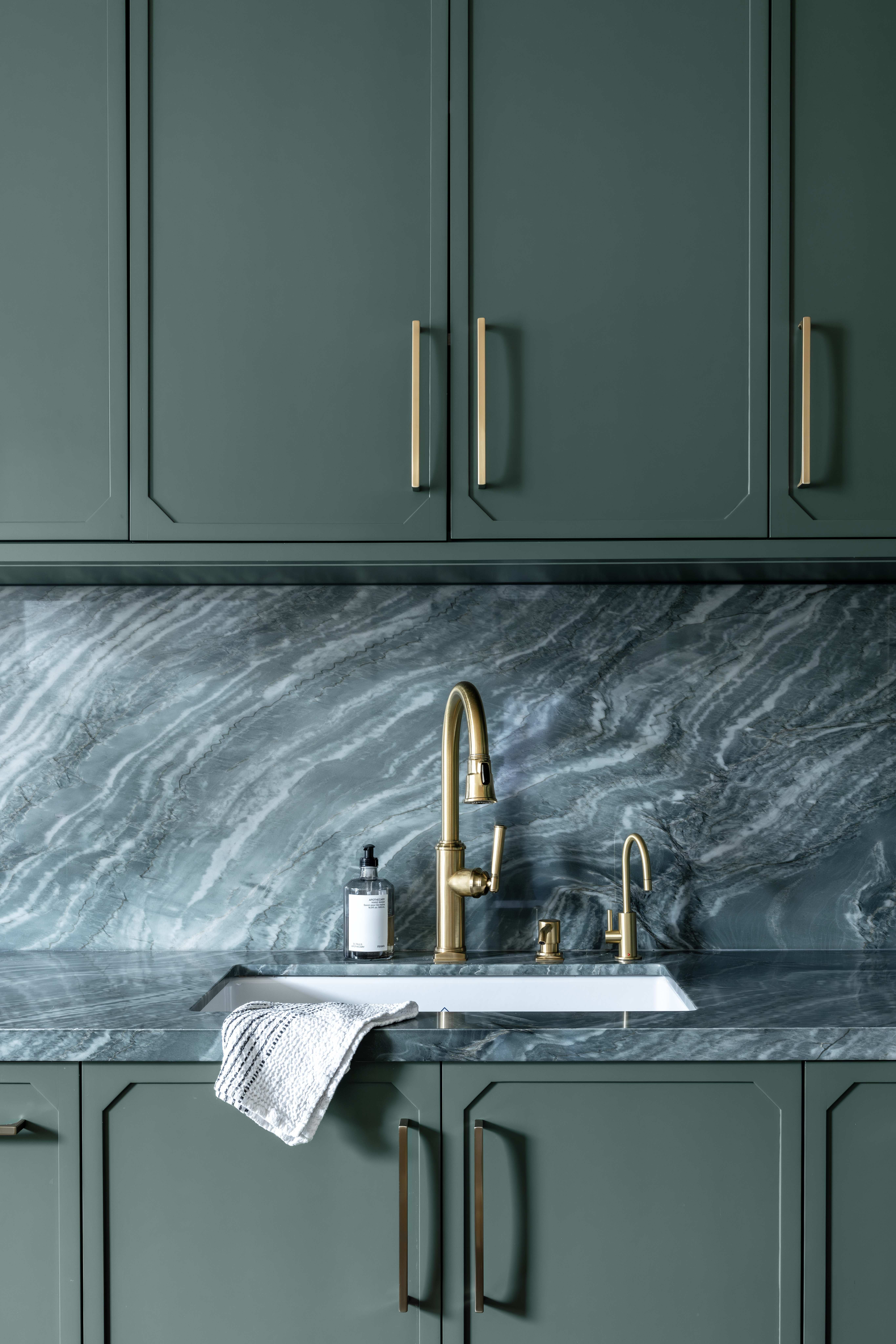 A kitchen with deep green cabinets and brass hadware