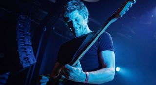 Lizzard's Mathieu Ricou smiles (or grimaces) as he takes a solo onstage, the stage illuminated in blue.