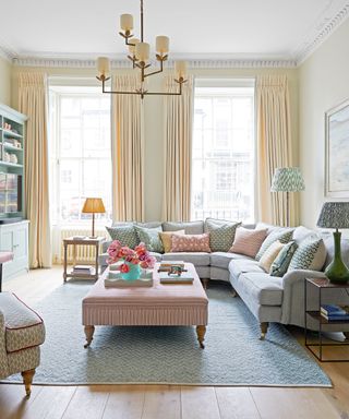 Elegant living room with gray corner sofa, cream curtains and cream walls, blue rug, large stiped ottoman, chandelier