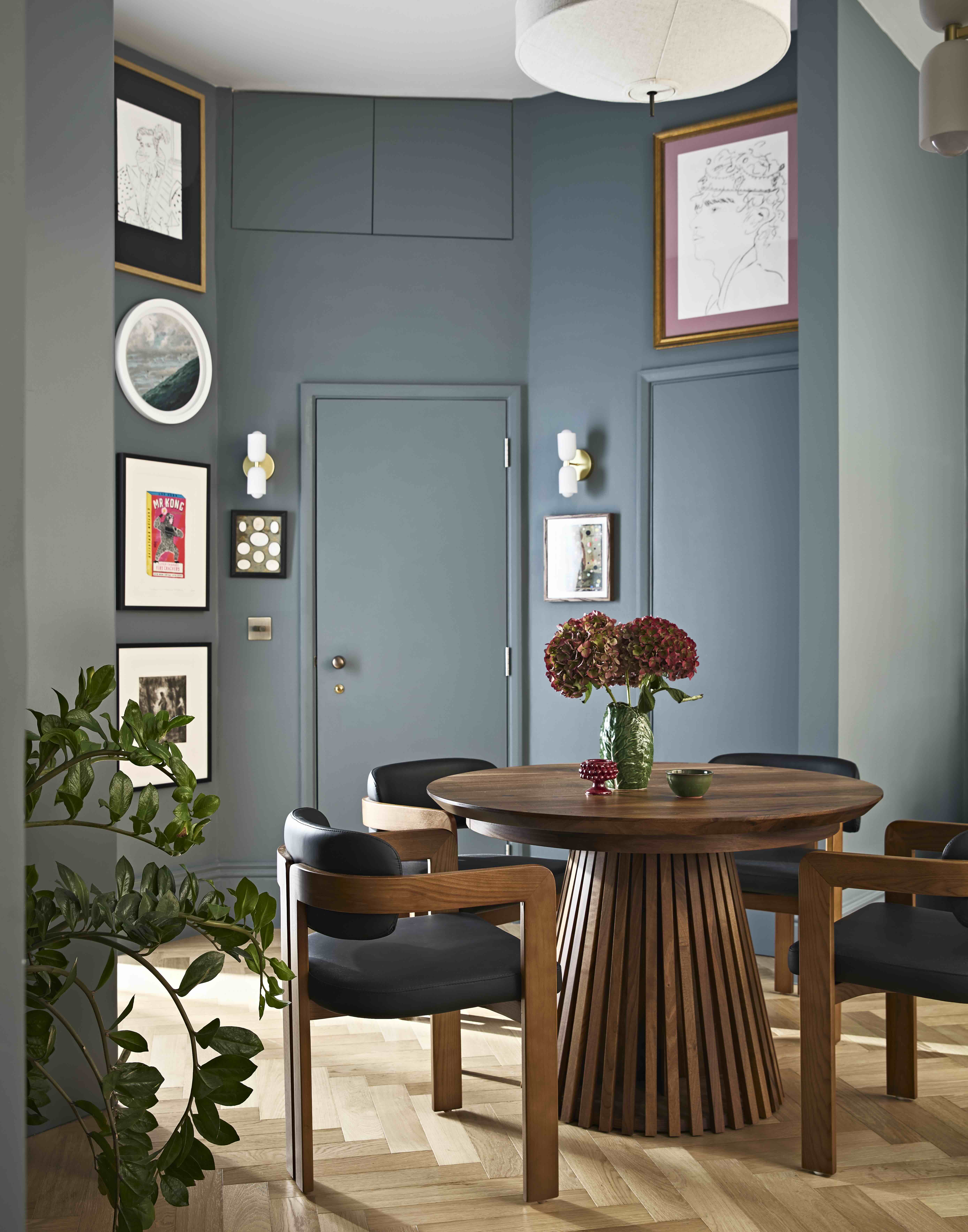 A small dining room in the hallway of an apartment, painted blue and filled with eclectic objects