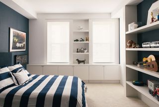 bedroom with dark blue wall and wide striped bedcovers and open shelves and windows