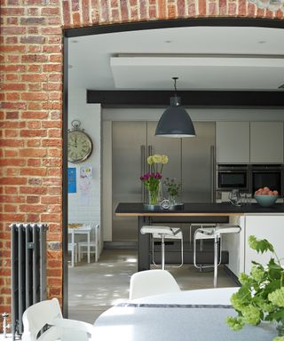 A view into a kitchen extension from outside with a brick arched doorway and a large gray pendant lamp above an island