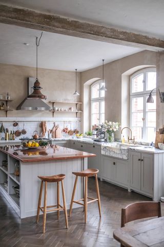 A farmhouse style kitchen with herringbone flooring, a large island with cream cabinets and two wooden bar stools