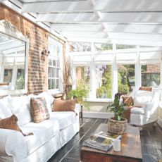 A white conservatory with a white sofa and armchair and an exposed brick wall