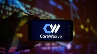 CoreWeave logo and branding pictured on a smartphone held aloft by a hand.