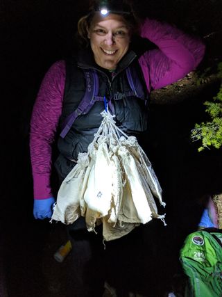 Catherine Haase, a postdoctoral researcher of wildlife ecology at Montana State University and modeling lead with the Wildlife Conservation Society, carries bags filled with bats so she can transport them down to the mobile laboratory.