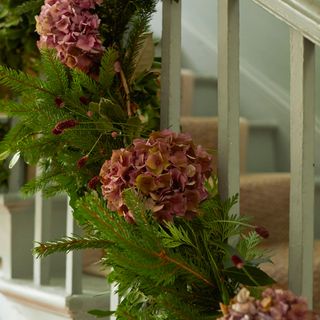 Foliage with pink Christmas roses tied to the handrail of a white staircase