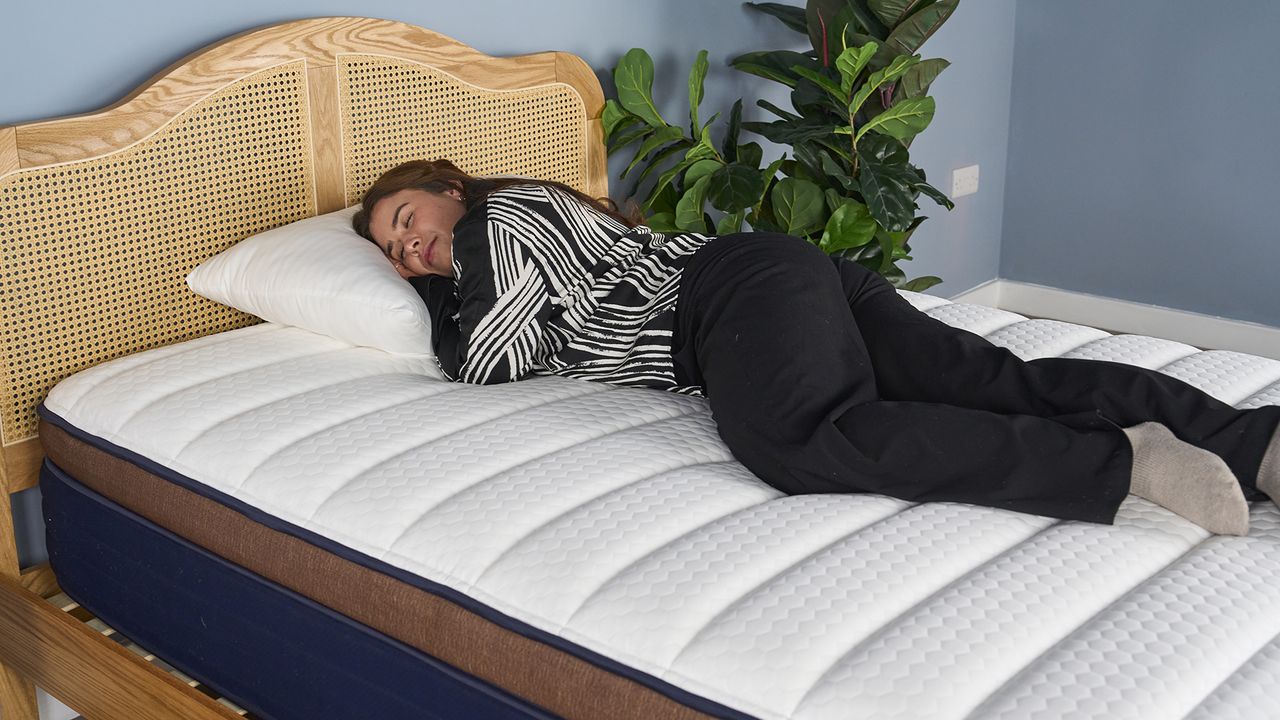 A girl wearing black and white pyjamas laying on her side on Brooklyn Bedding CopperFlex Pro Hybrid mattress with white surface and rattan bedframe