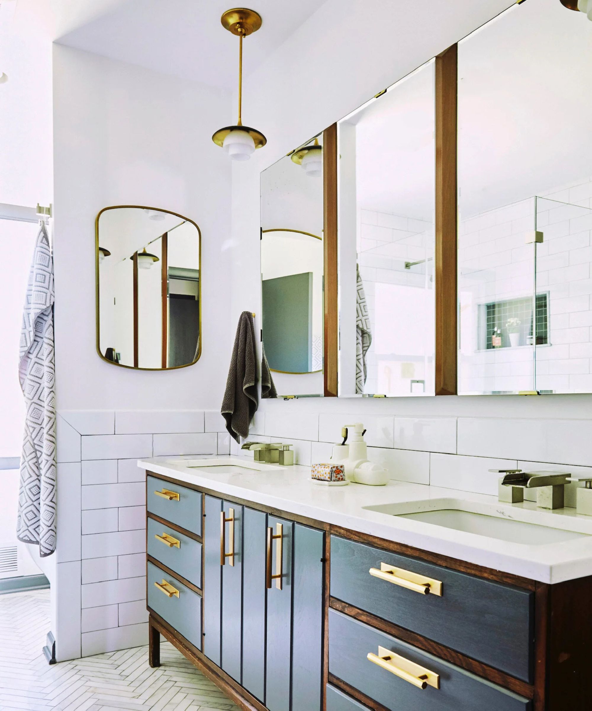 A mid-century modern inspired double bathroom vanity with a blue and dark wood unit, three medicine cabinets, and a pendant light above