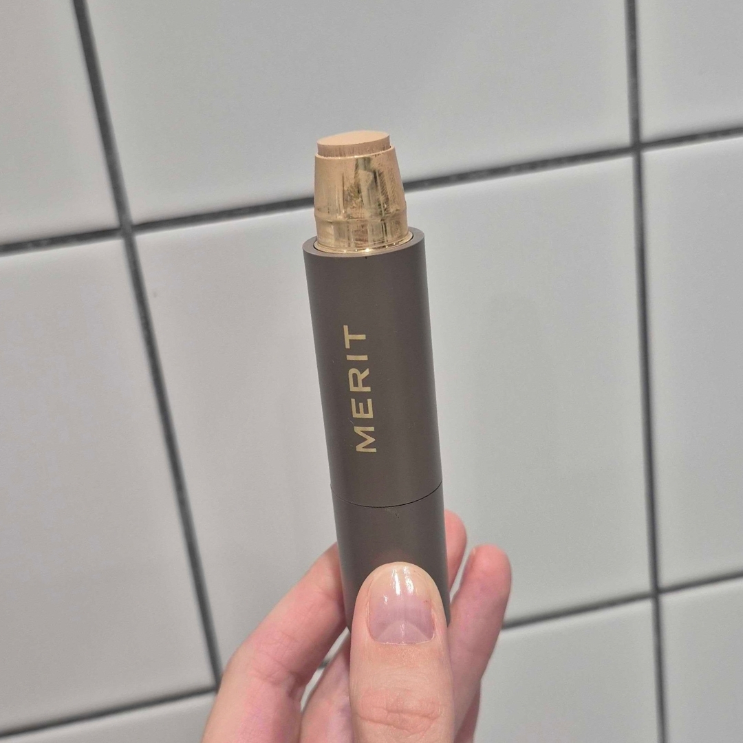 Hand holding empty tube of Merit Beauty The Minimalist Stick