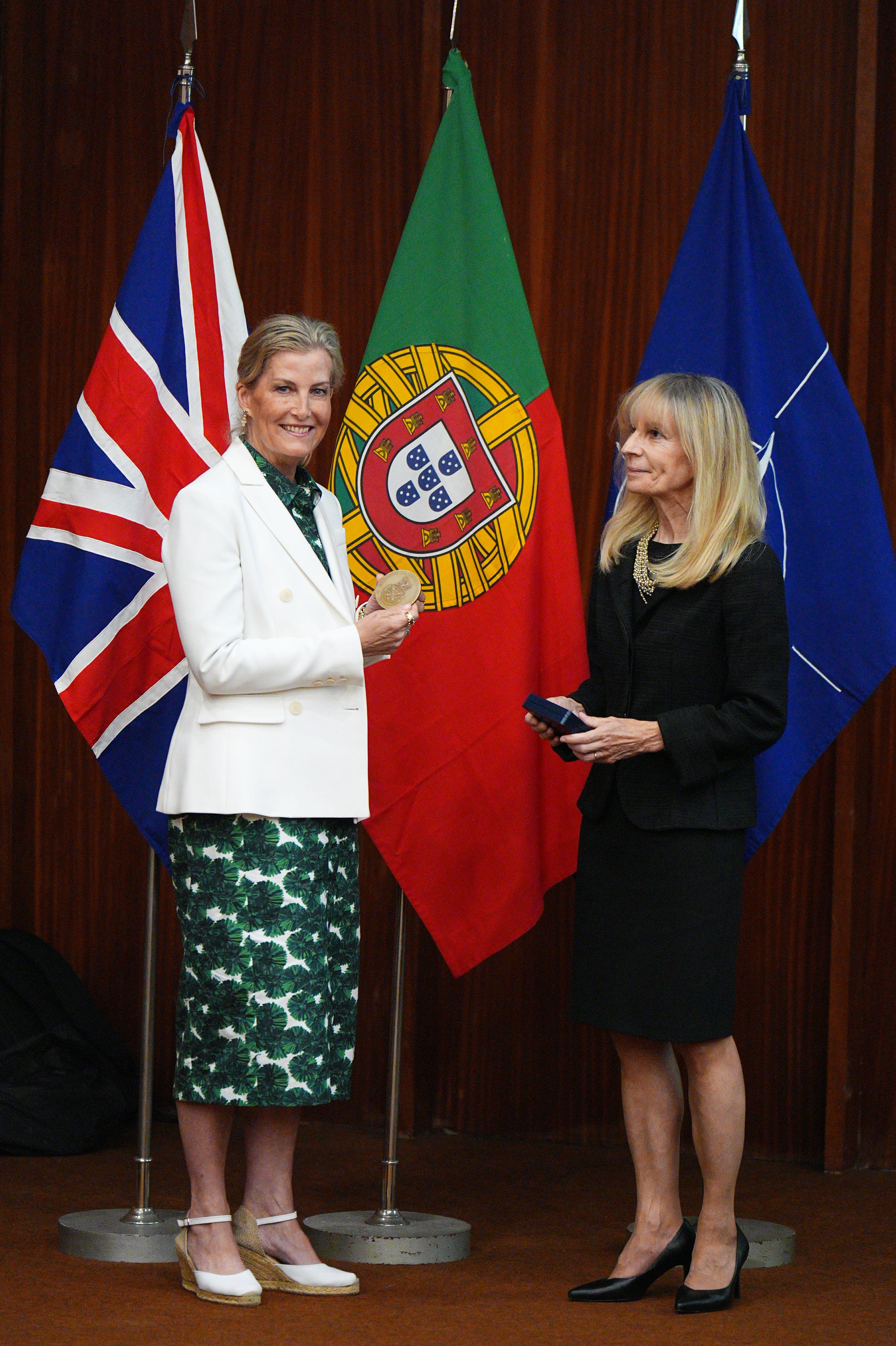 Duchess Sophie wearing a white blazer and green dress standing in front of flags with a woman