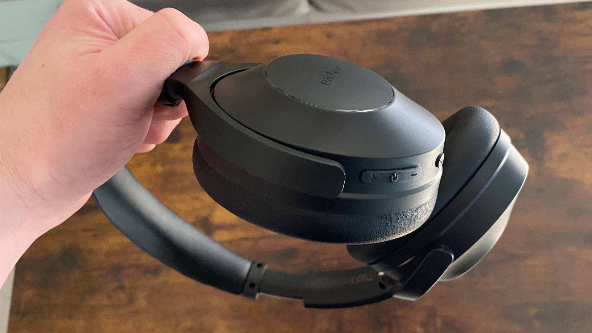 Earfun Wave Life over-ear headphones, folded inwards, held in-hand over a wooden surface