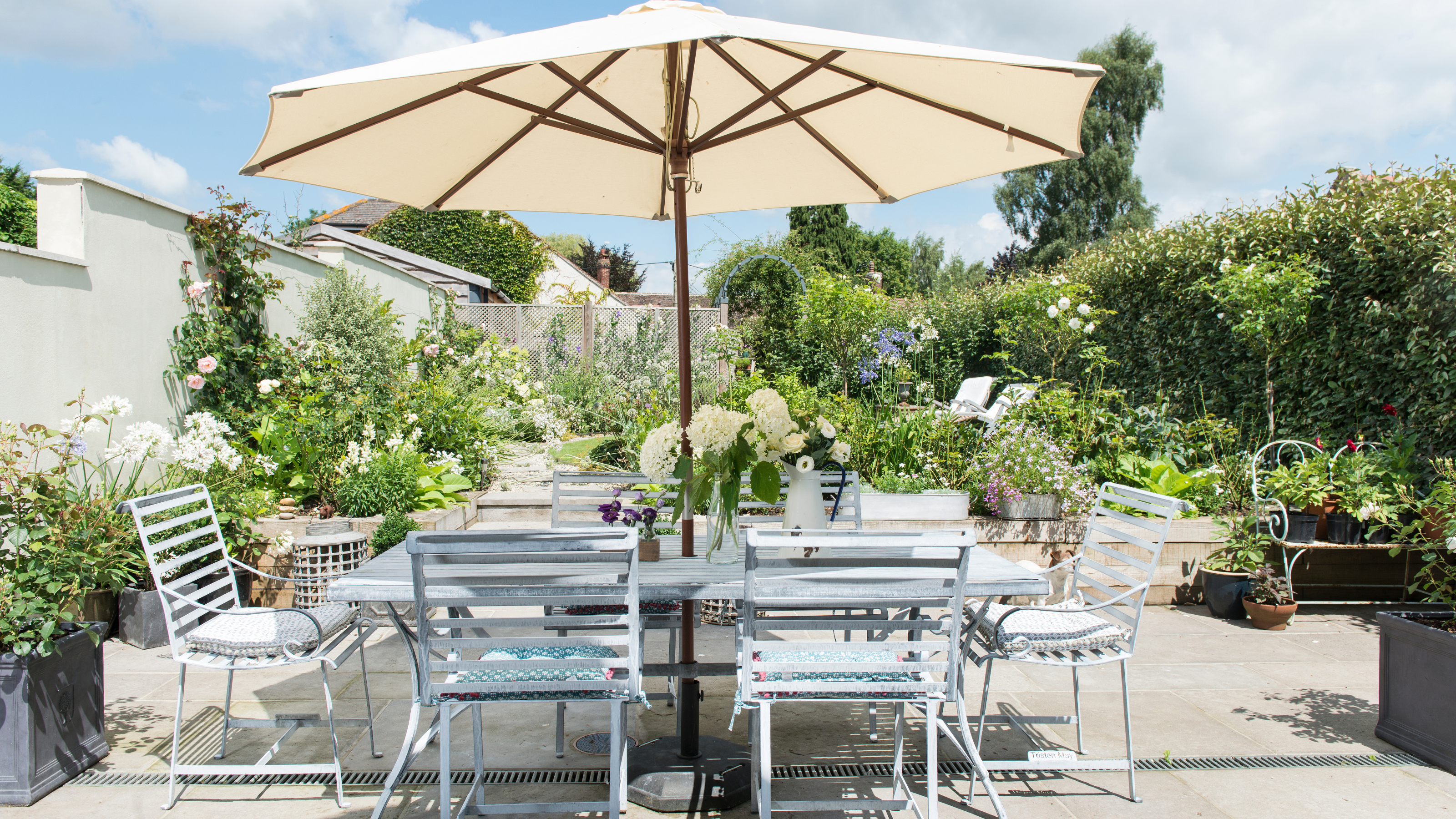 A seating area in a terraced garden, dining table and chairs and large parasol.