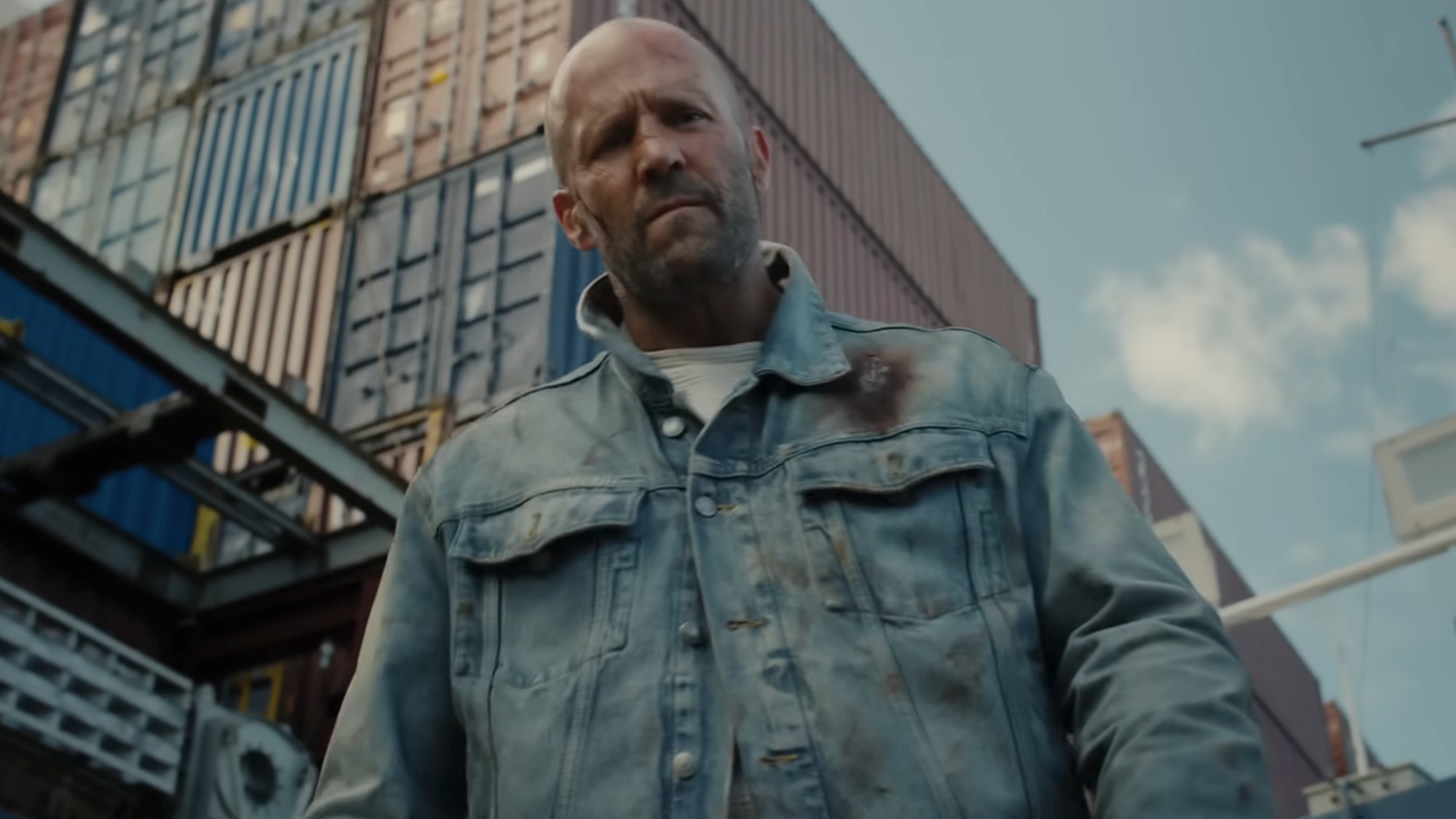 Jason Statham in a dirty denim jacket looking down towards the camera below him
