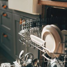 Open dishwasher with loaded top drawer pulled out in a kitchen with grey blue cupboards and a butlers sink