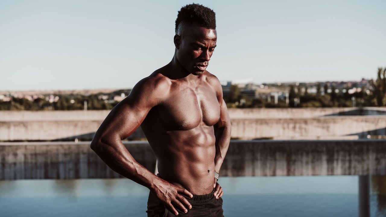 Person standing on the edge of a lake shirtless, displaying his chiseled abdominal area