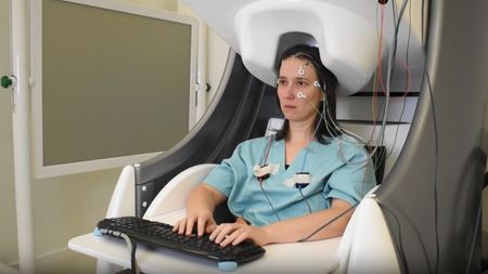 A women sits in a chair with wires on her head while typing on a keyboard.