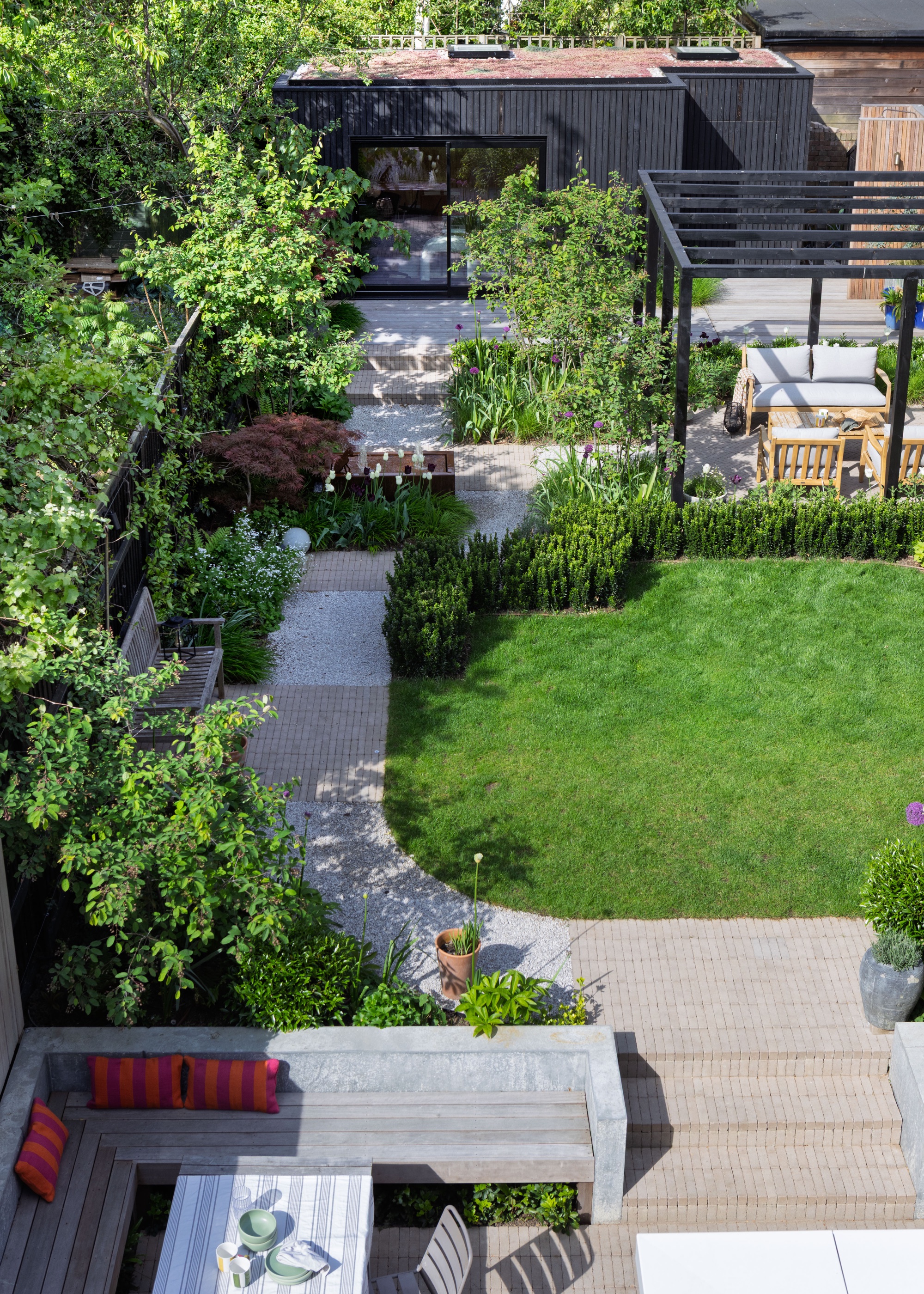 zoned garden with separate dining, lawn, lounging, and pergola spaces in a backyard. there is also a built in seating area in one side of the garden