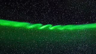 A streak of green light in the night sky with ripples running through the middle