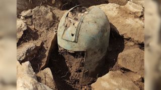 2500-year-old metal helmet amongst rocks and dirt.