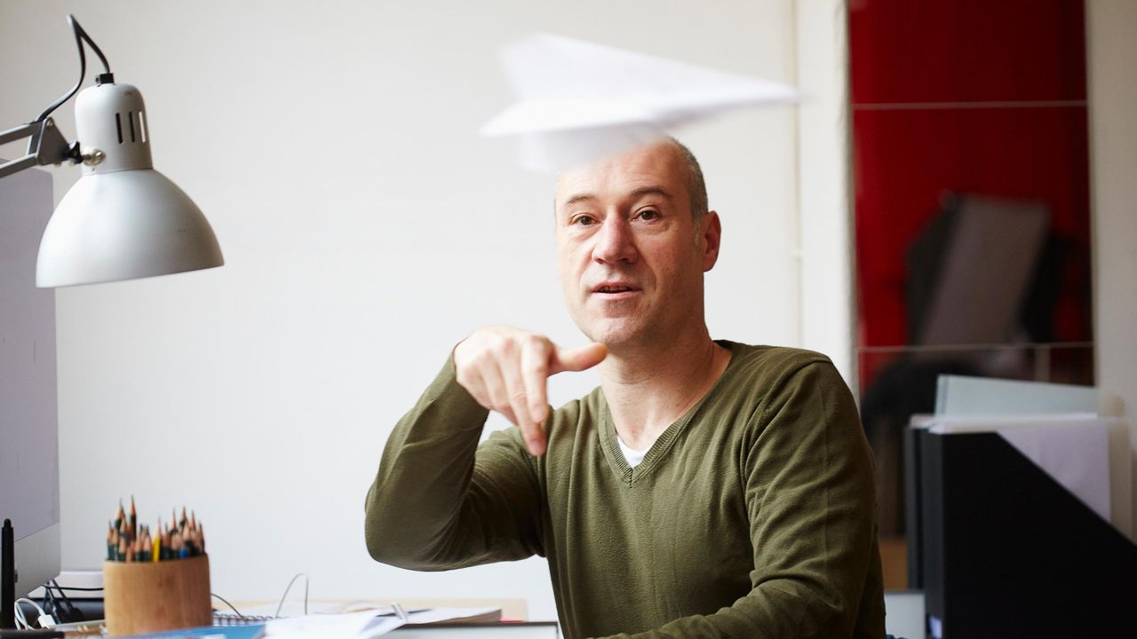 A man at a desk wastes time by throwing a paper airplane.