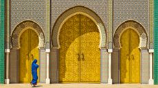 A woman in a blue outfit walks in front of a golden door at the Royal Palace in Fez, Morocco