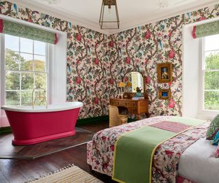 red sided roll top bath in bedroom with red and green floral wallpaper