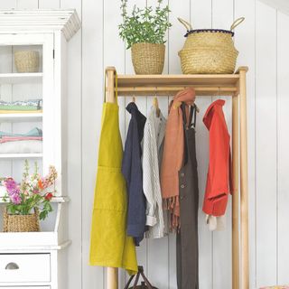 An open wooden wardrobe with a few clothes hanging from it, with woven baskets sitting on top of it