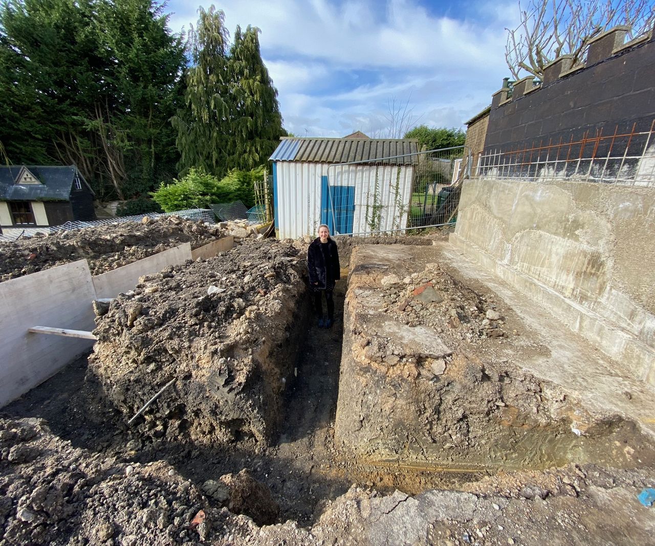 Woman standing in dug trenches for foundations to be laid for a new extension