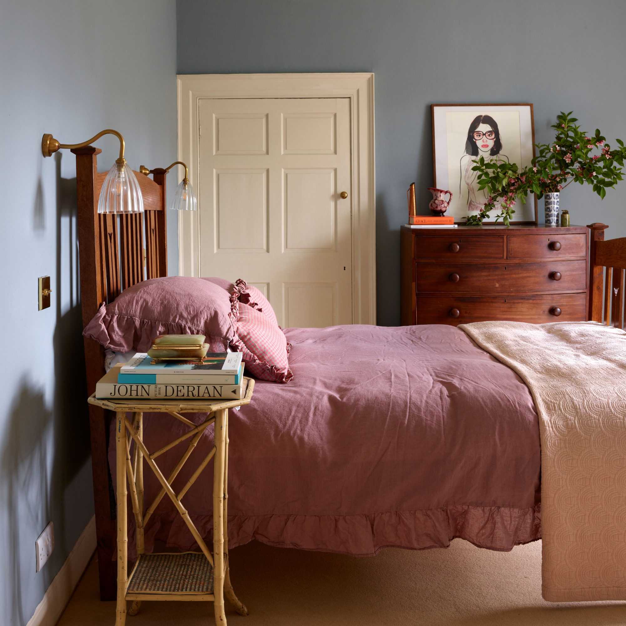 Painted bedroom with pink bedding on cane bedframe, dresser, bedside table