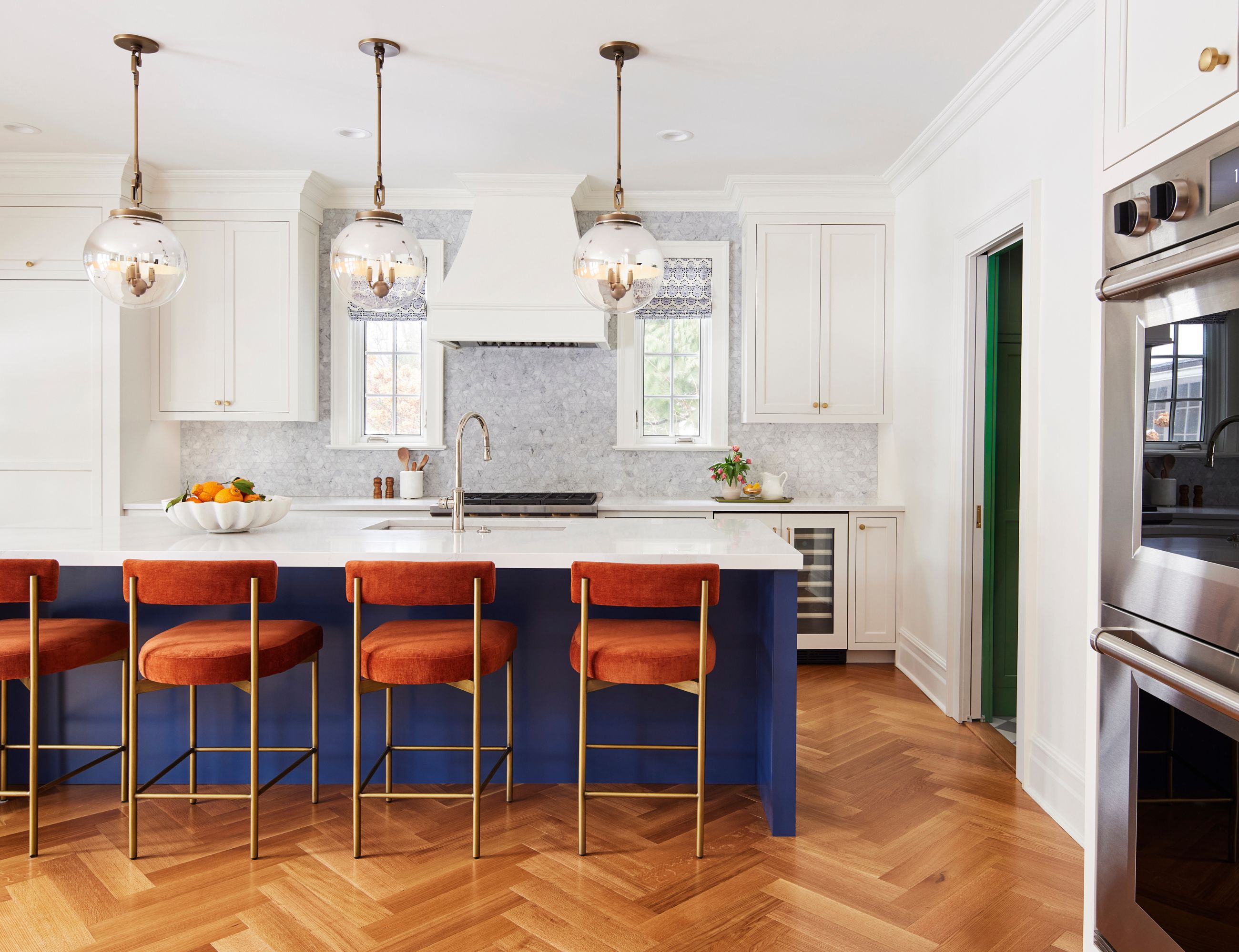 White kitchen with dark blue kitchen island and orange velvet seating