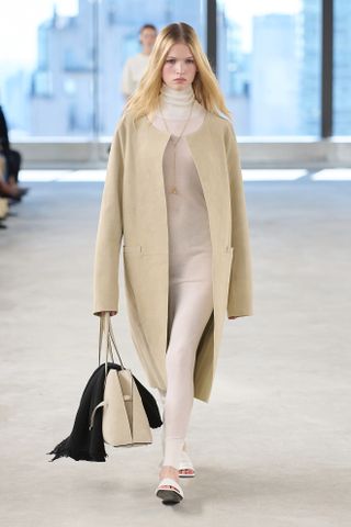 A Toteme model walks the spring/summer 2025 runway wearing a collarless coat.