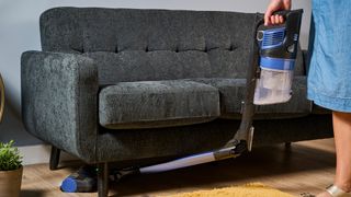 Shark cordless vacuum with wand bent forward, vacuuming beneath a sofa