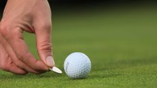Close up of a golfer placing a marker behind a golf ball on the putting green